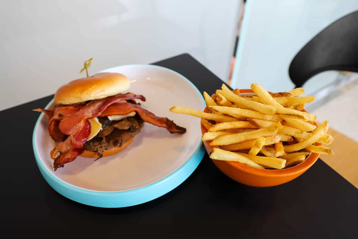 the burger topped with bacon and cheese on the left side next to a bowl of fried 