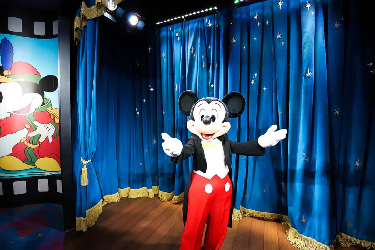 Mickey in suit and tie in front of blue curtains with stars. 