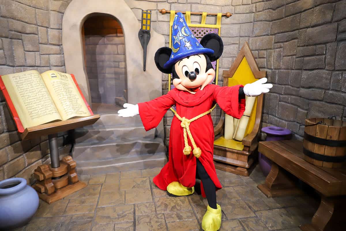 Mickey Mouses poses in his red sorcerer robe and blue hat. 
