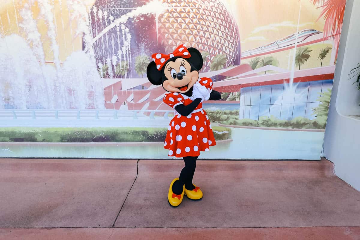 Minnie Mouse poses in front of a Spaceship Earth Mural. 