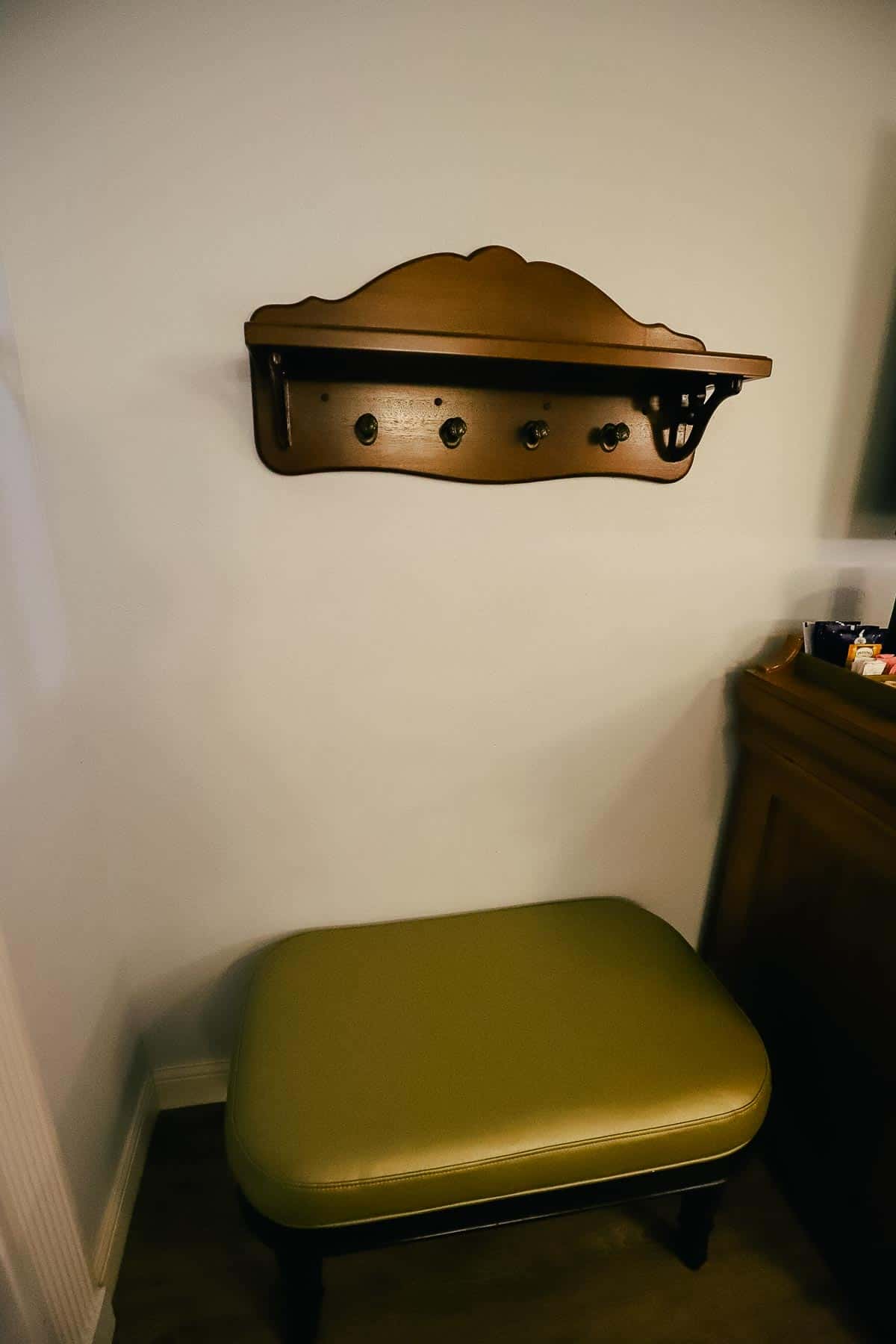 a shelf with places to hang items underneath it and a bench with a green top