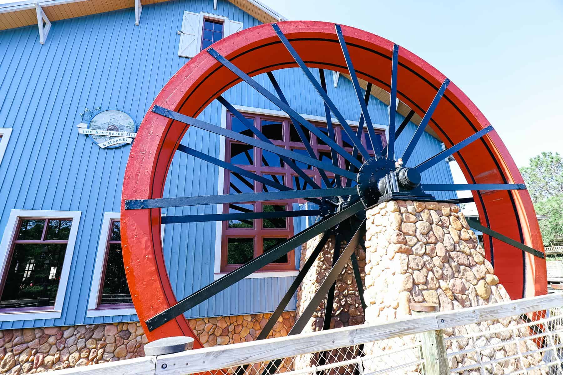 a red working water wheel in front of a blue building 