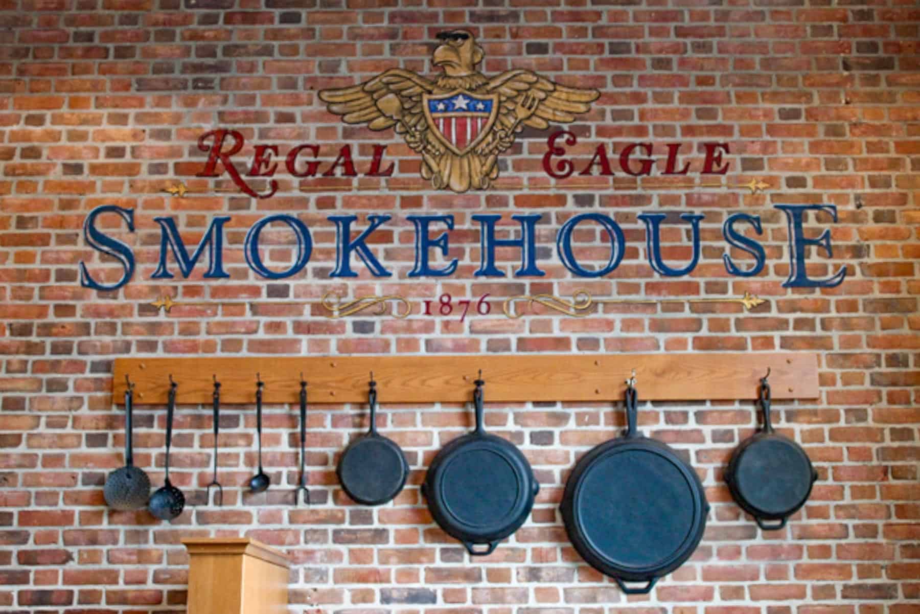 a brick wall with cast iron skillets hanging underneath lettering that says Regal Eagle Smokehouse 