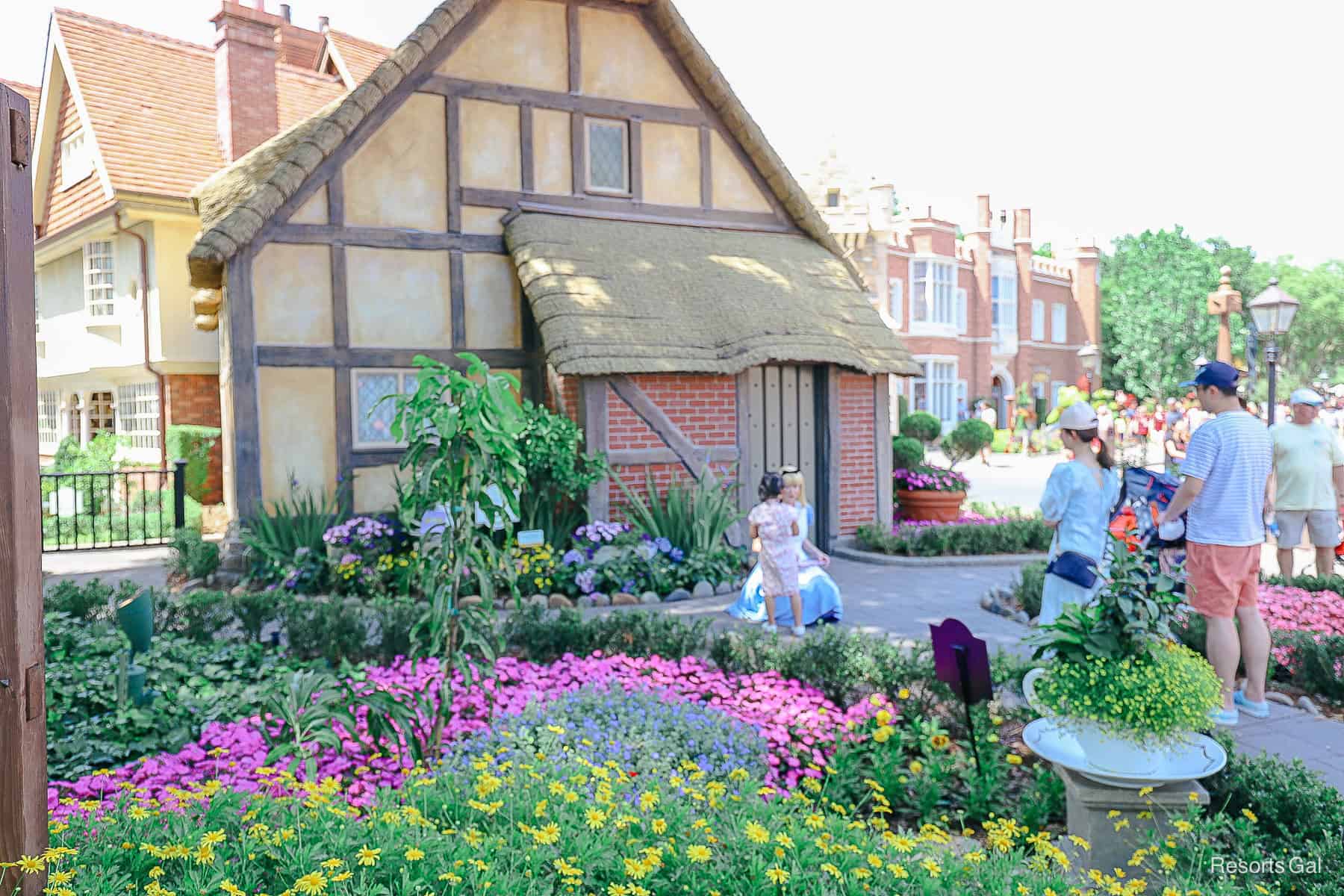 Alice greets guests in front of a cottage (tea shop) 