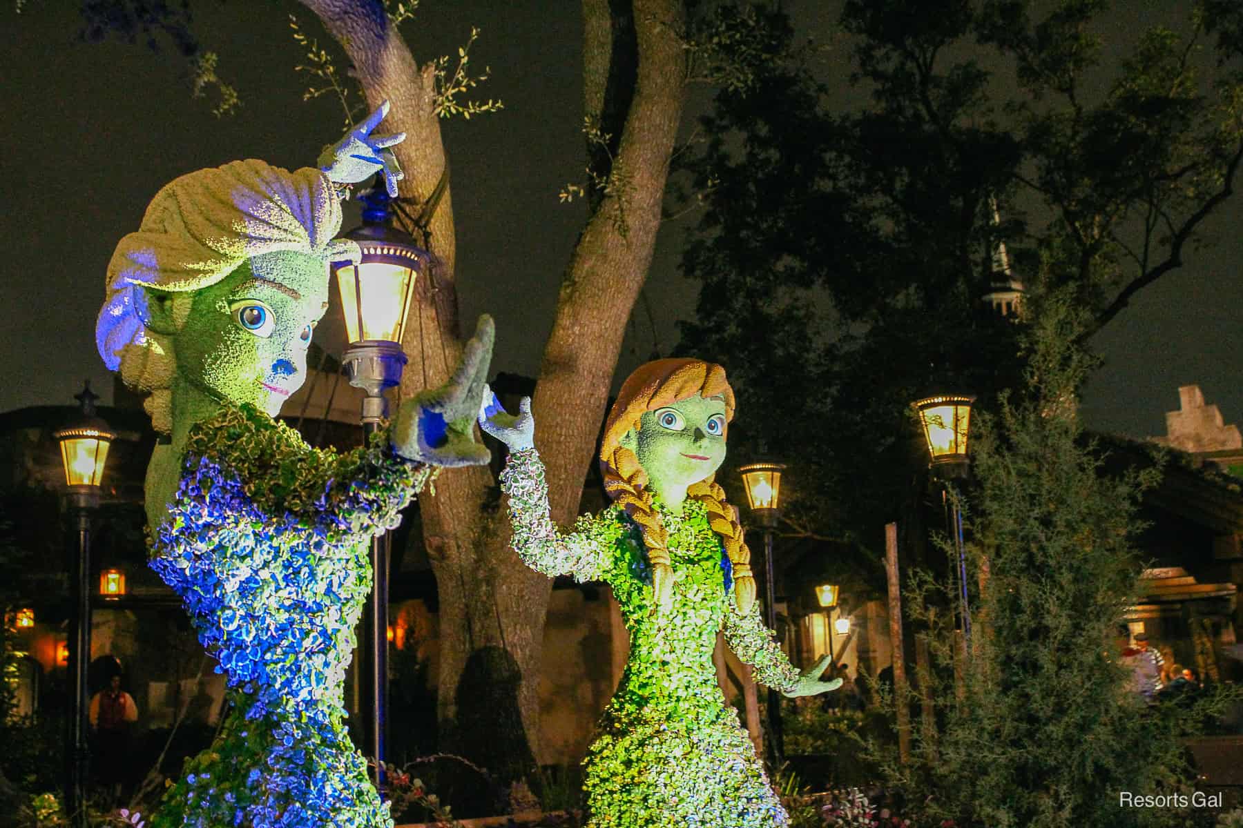 Anna and Elsa Character Topiaries at night surrounded by light poles