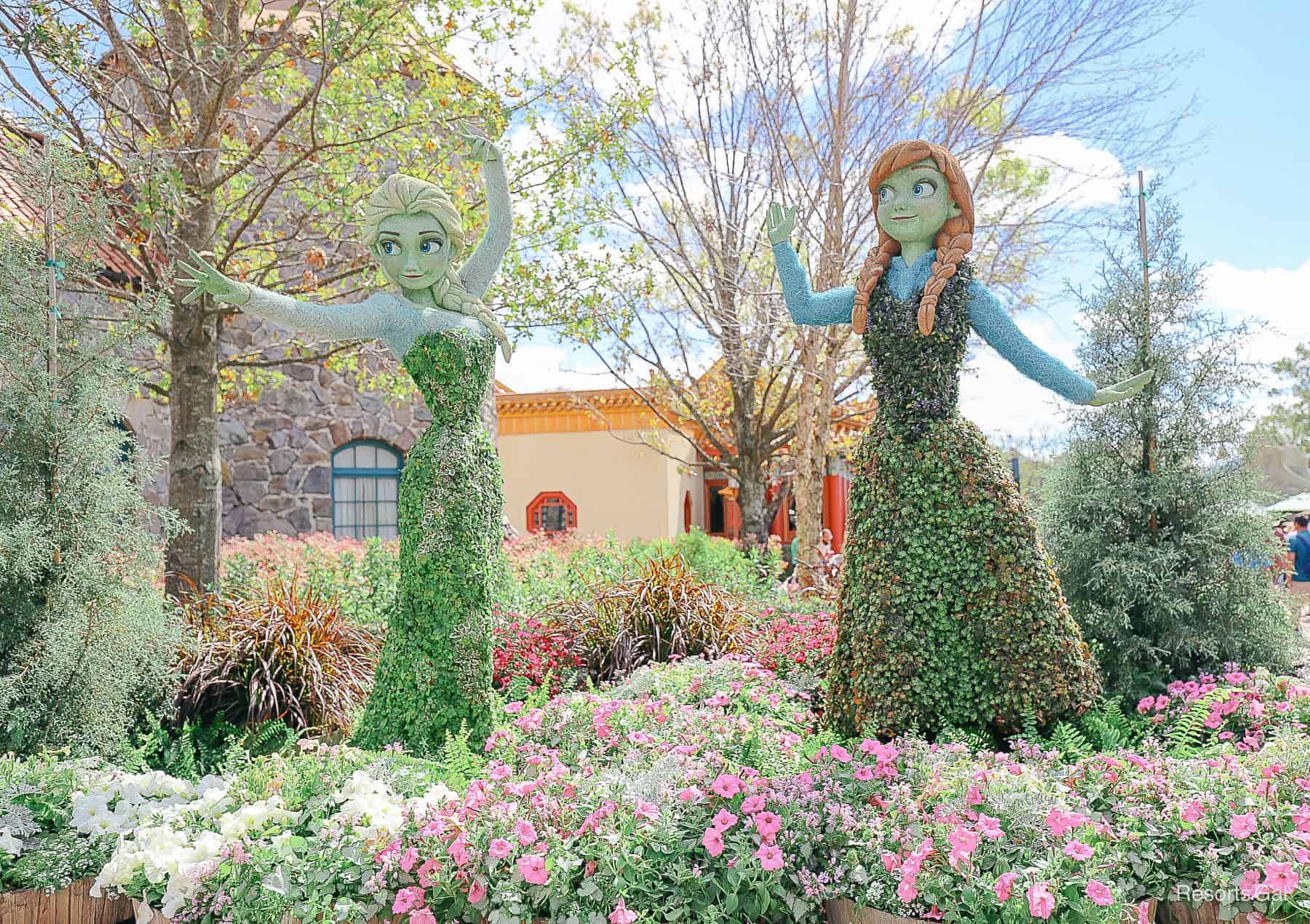 Elsa with arms extended and Anna waving in topiary form. 