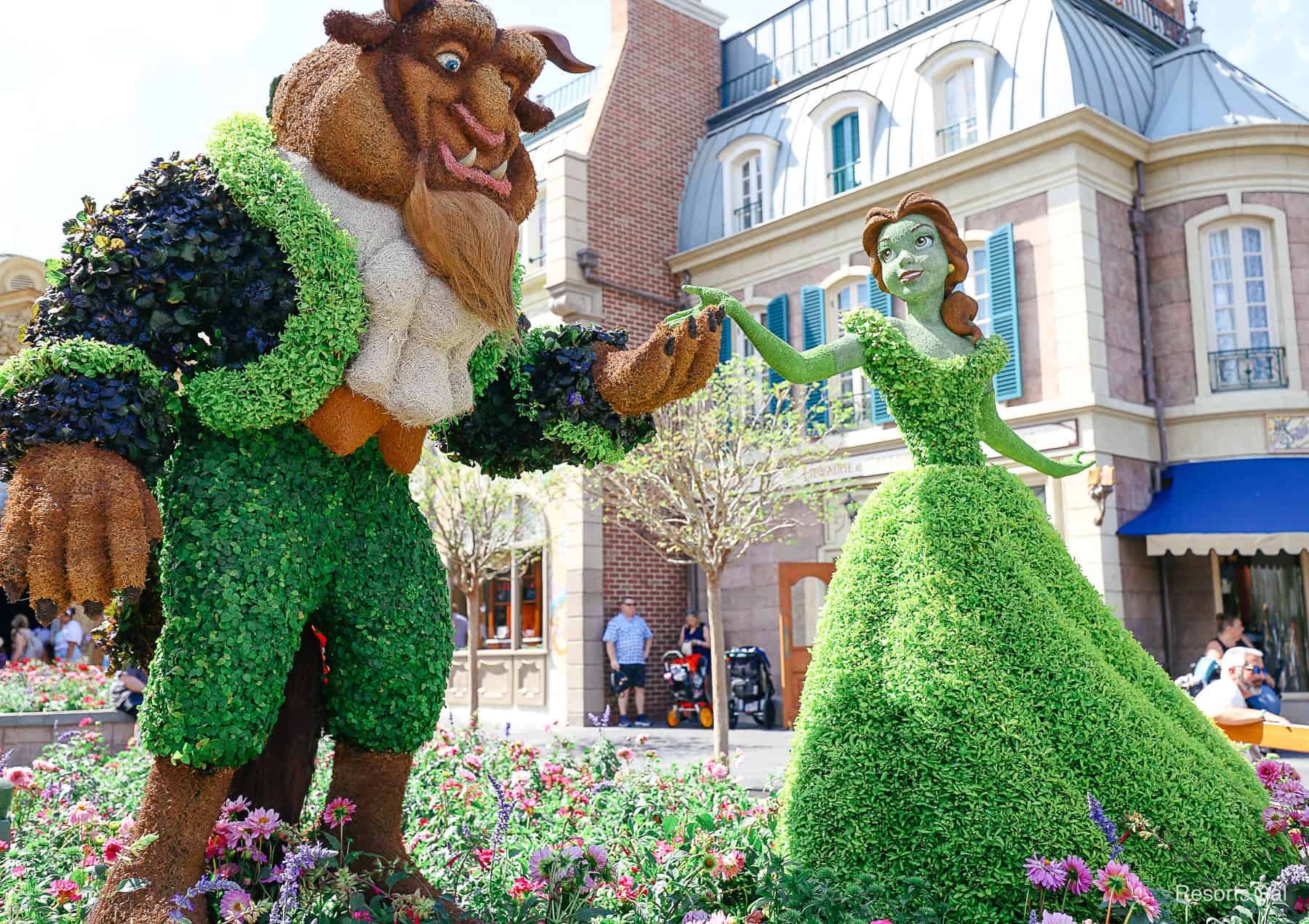 side angle of Belle's topiary looking to Beast's as he extends a hand 