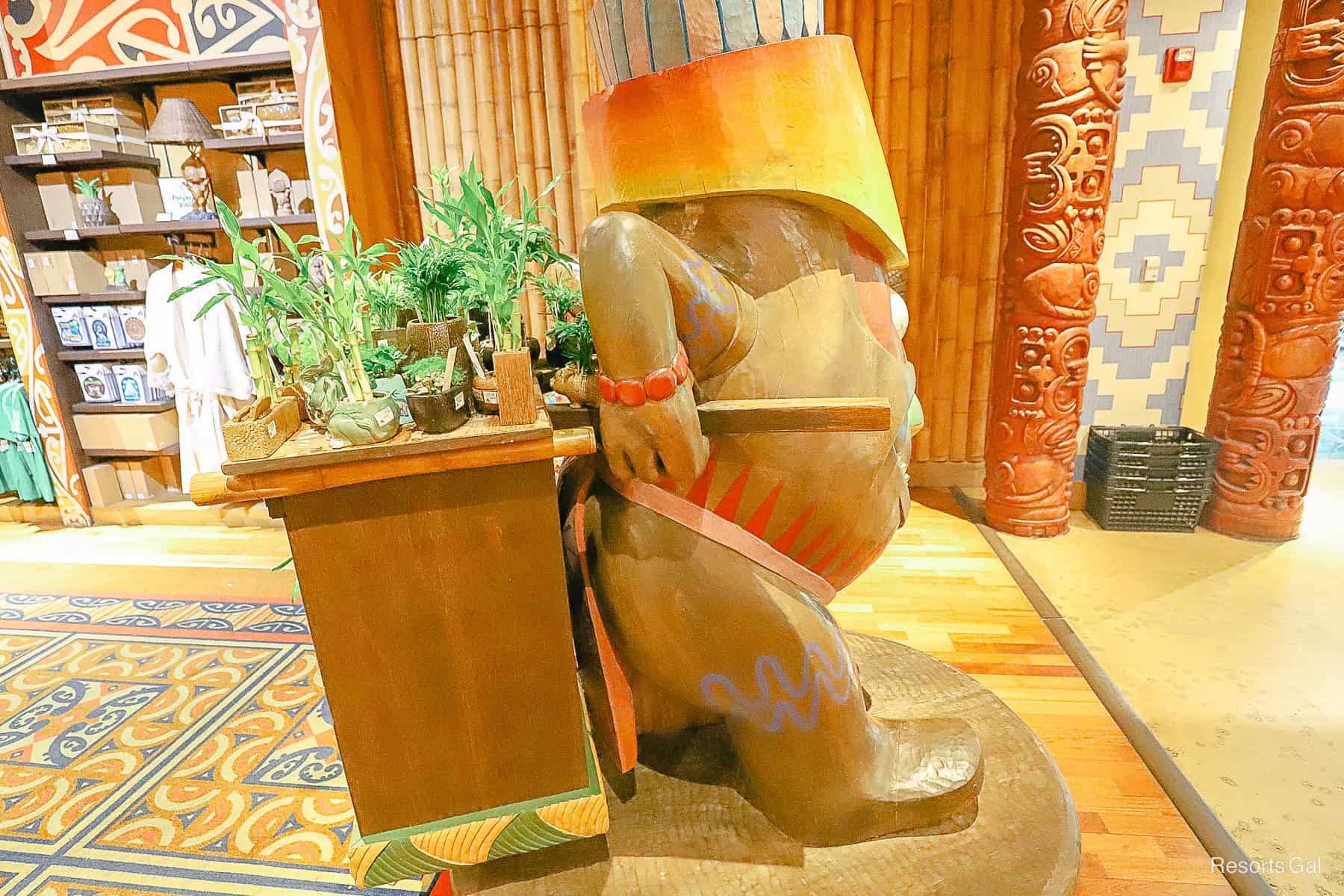 a Tiki statue display who appears to be carrying a load of small potted plants 