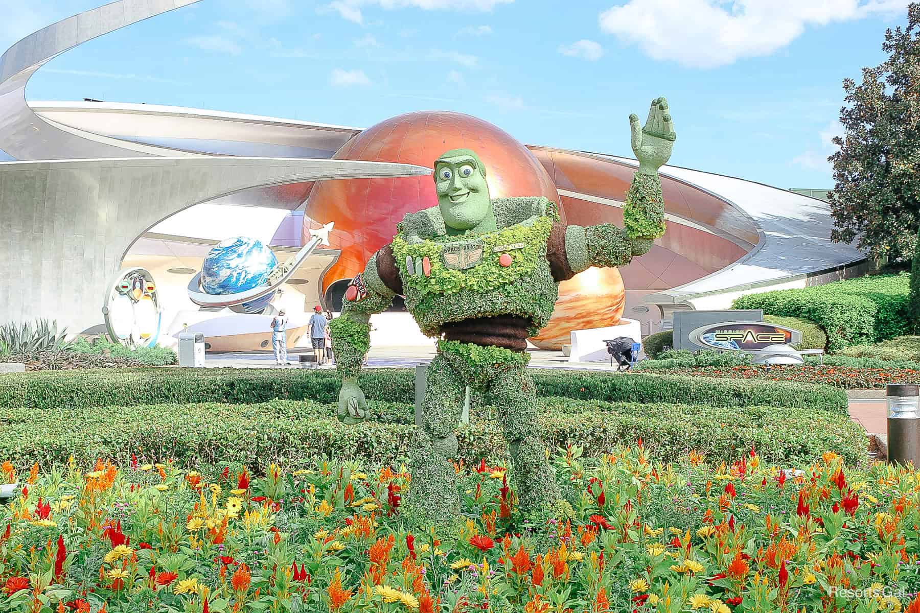 Buzz Lightyear in front of Mission: Space in topiary surrounded by red, yellow, and orange flowers