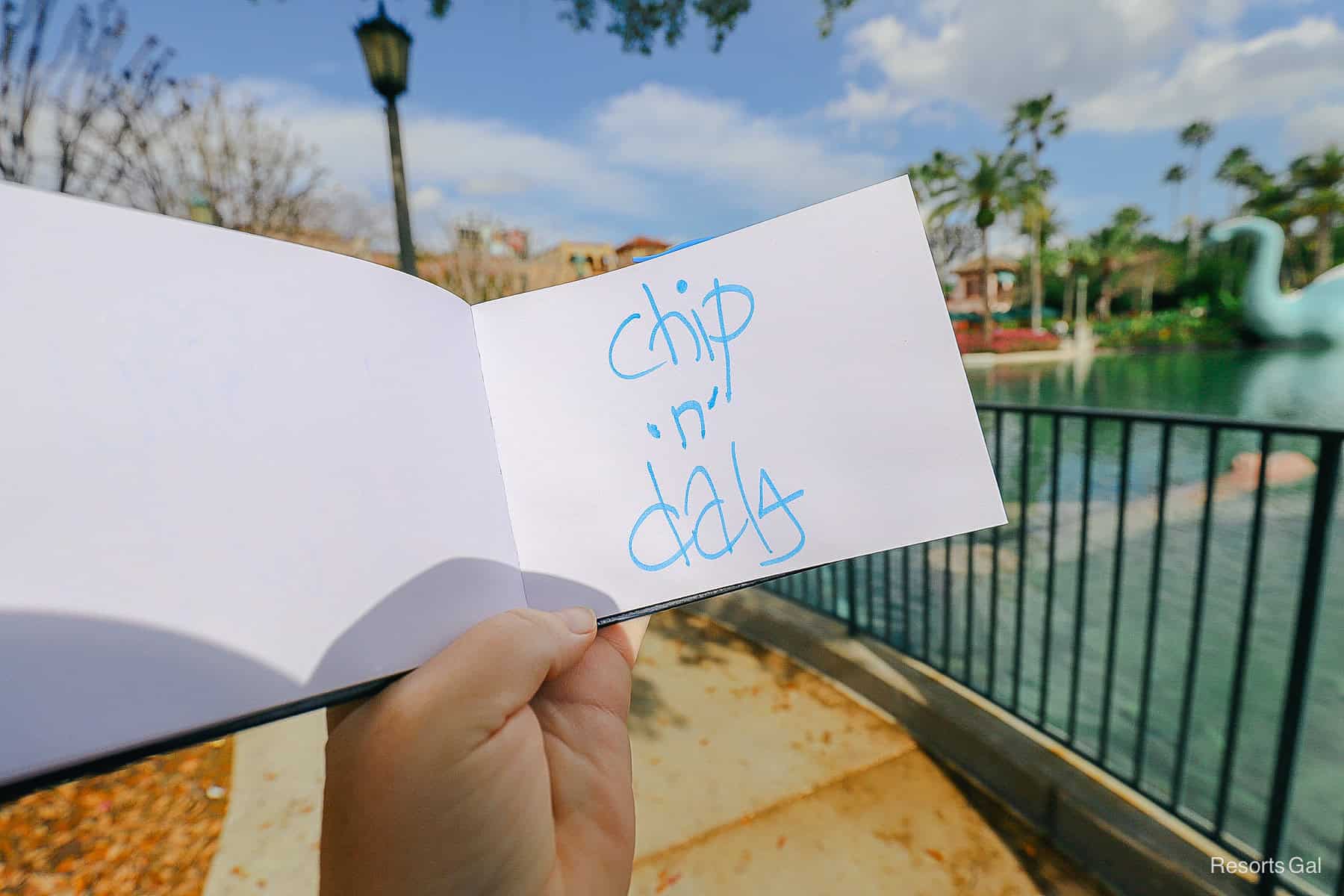 a hand holding an autograph book open with Chip n' Dale's signature 
