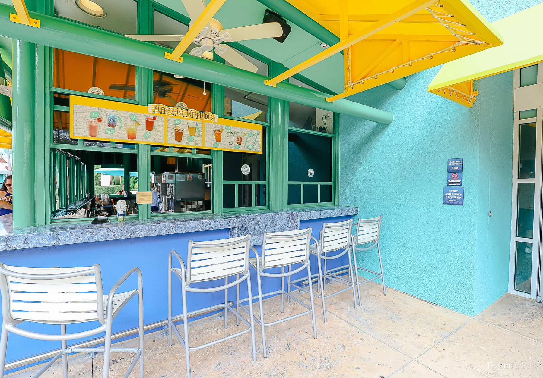 bar stools at the outdoor bar near the pool at All-Star Music with signage that says Refreshing Interludes 