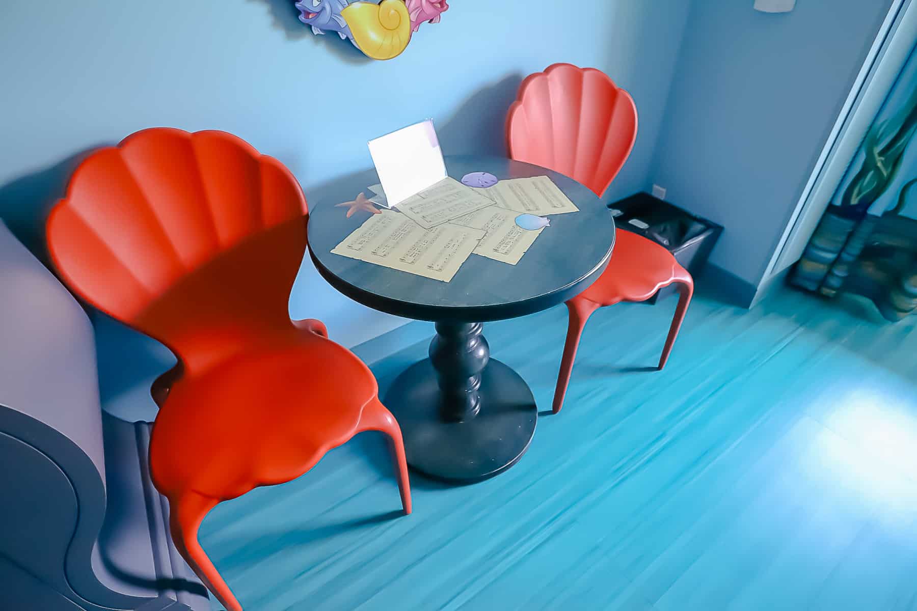 A pair of coral red chairs with a black table on blue solid surface floors. 