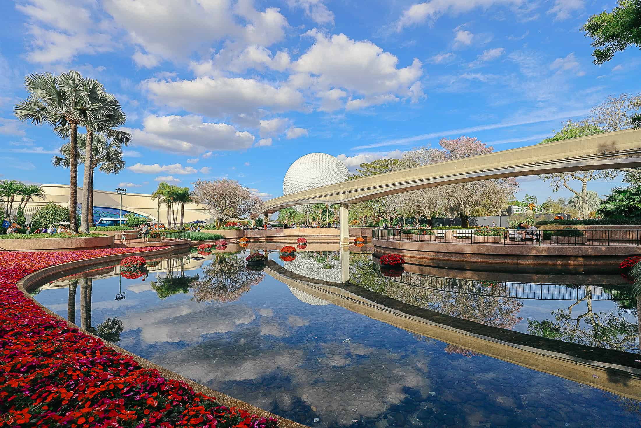 a lake with Epcot's icon Spaceship Earth in the backdrop with red flowers and blue skies 
