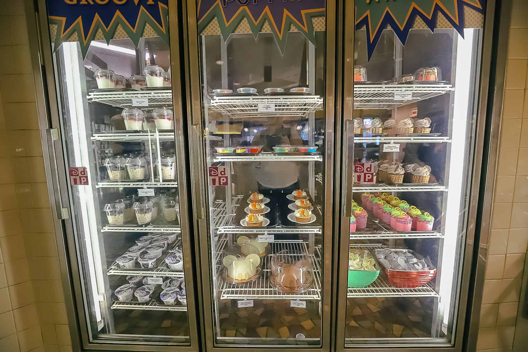 a refrigerated case with yogurt, cakes, cupcakes and other dessert items 