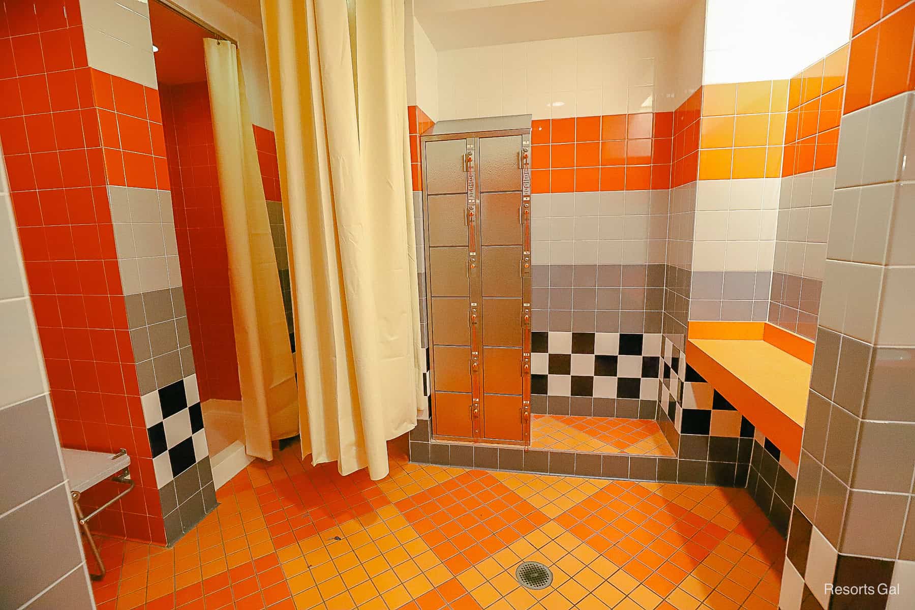 a pool changing area with orange, grey, and black tile with a stack of metal lockers 