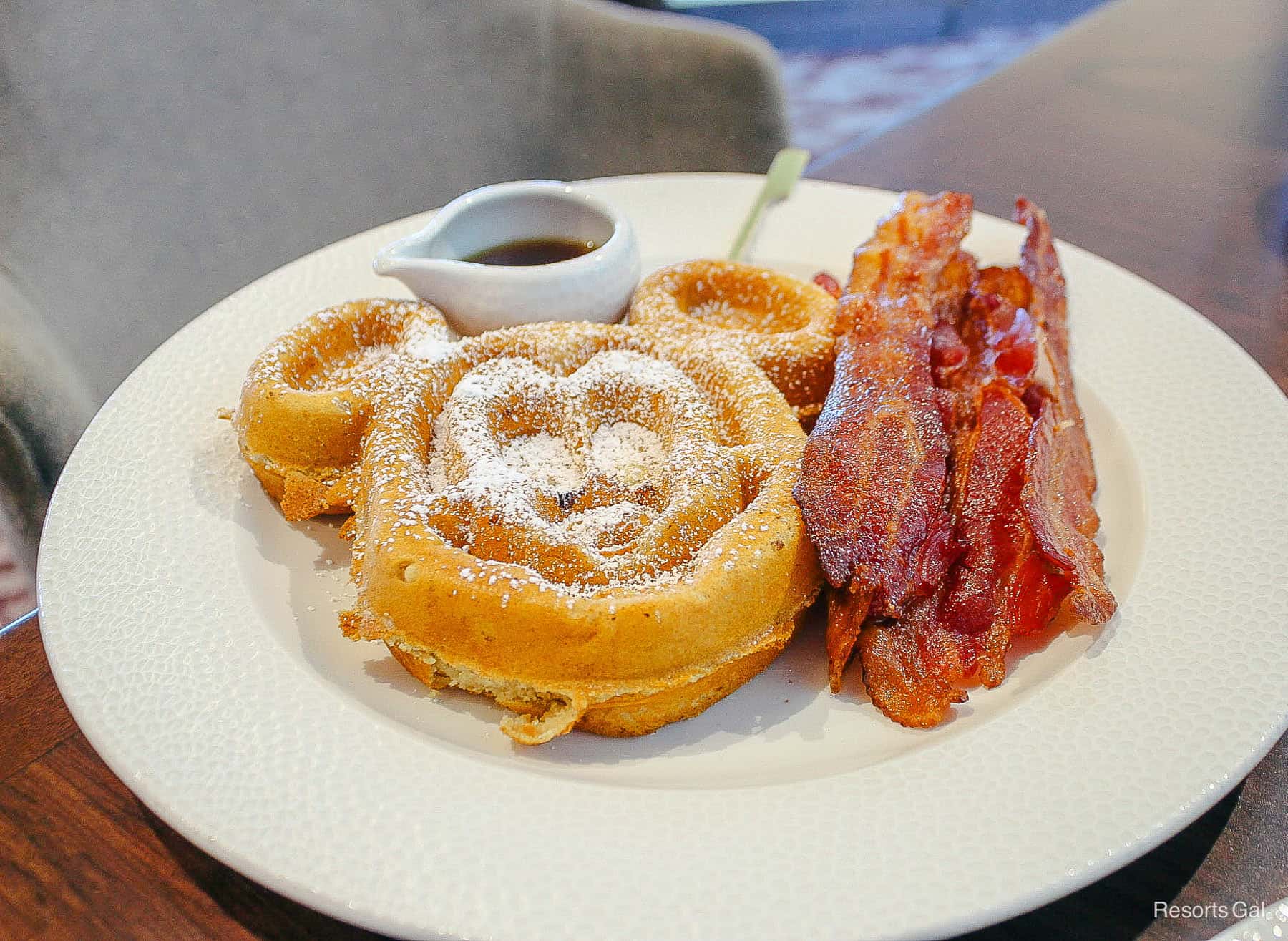 a large mickey-shaped sour cream waffle with a side of bacon 