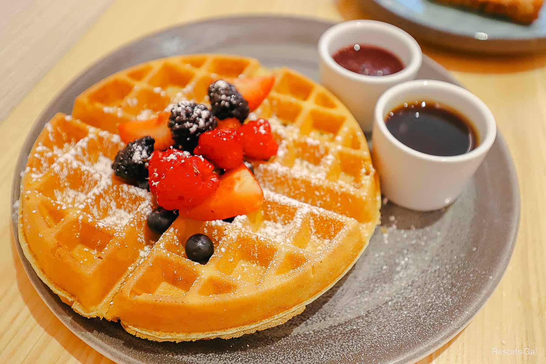 a freshly prepared waffles toped with berries and two syrups on the side. 