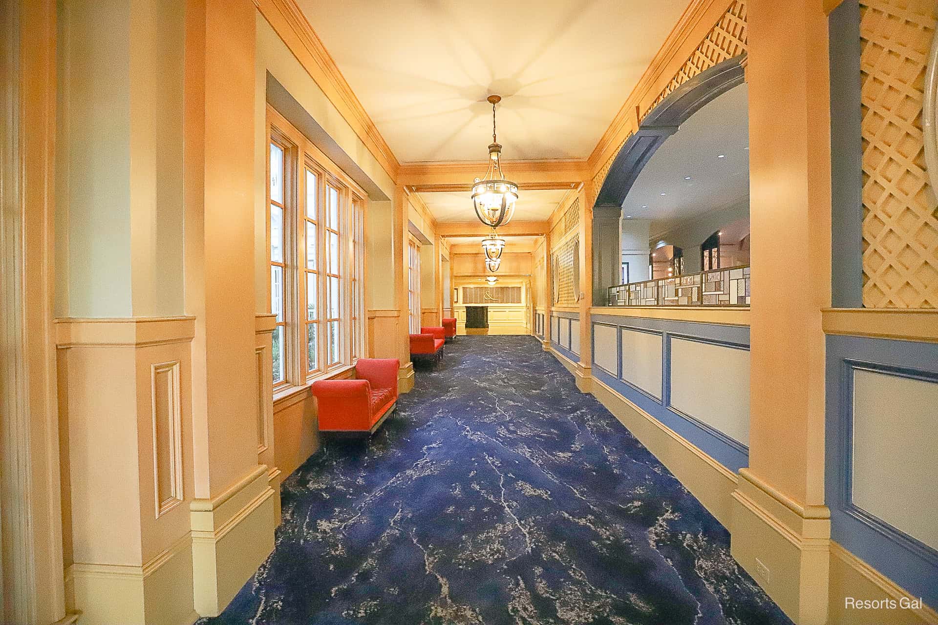 a sloped hallway with blue carpet and red benches 