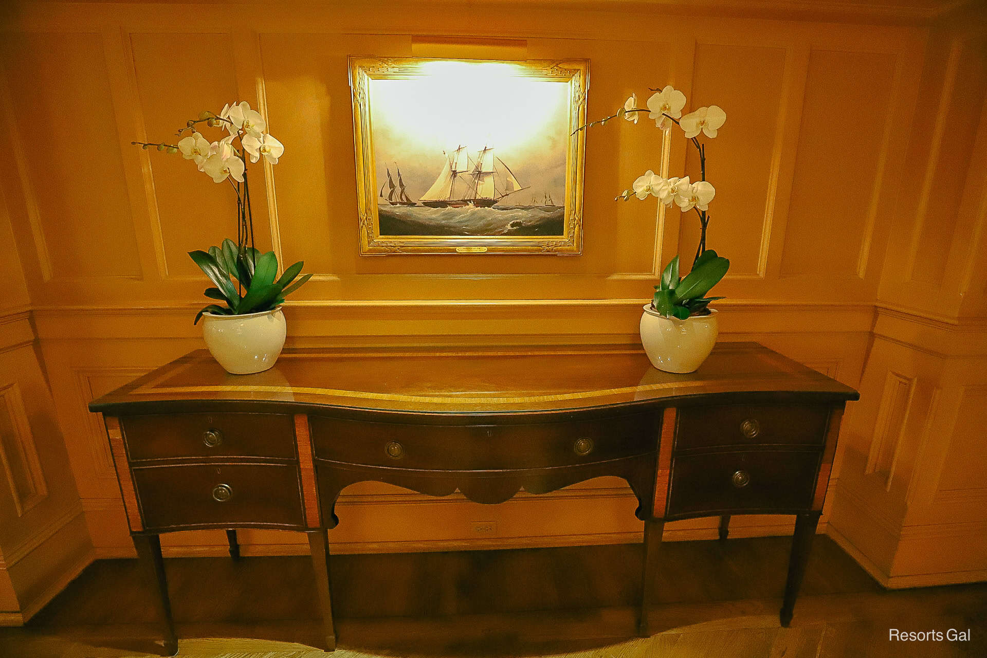 a hall table with two potted orchids and a ship painting over it 