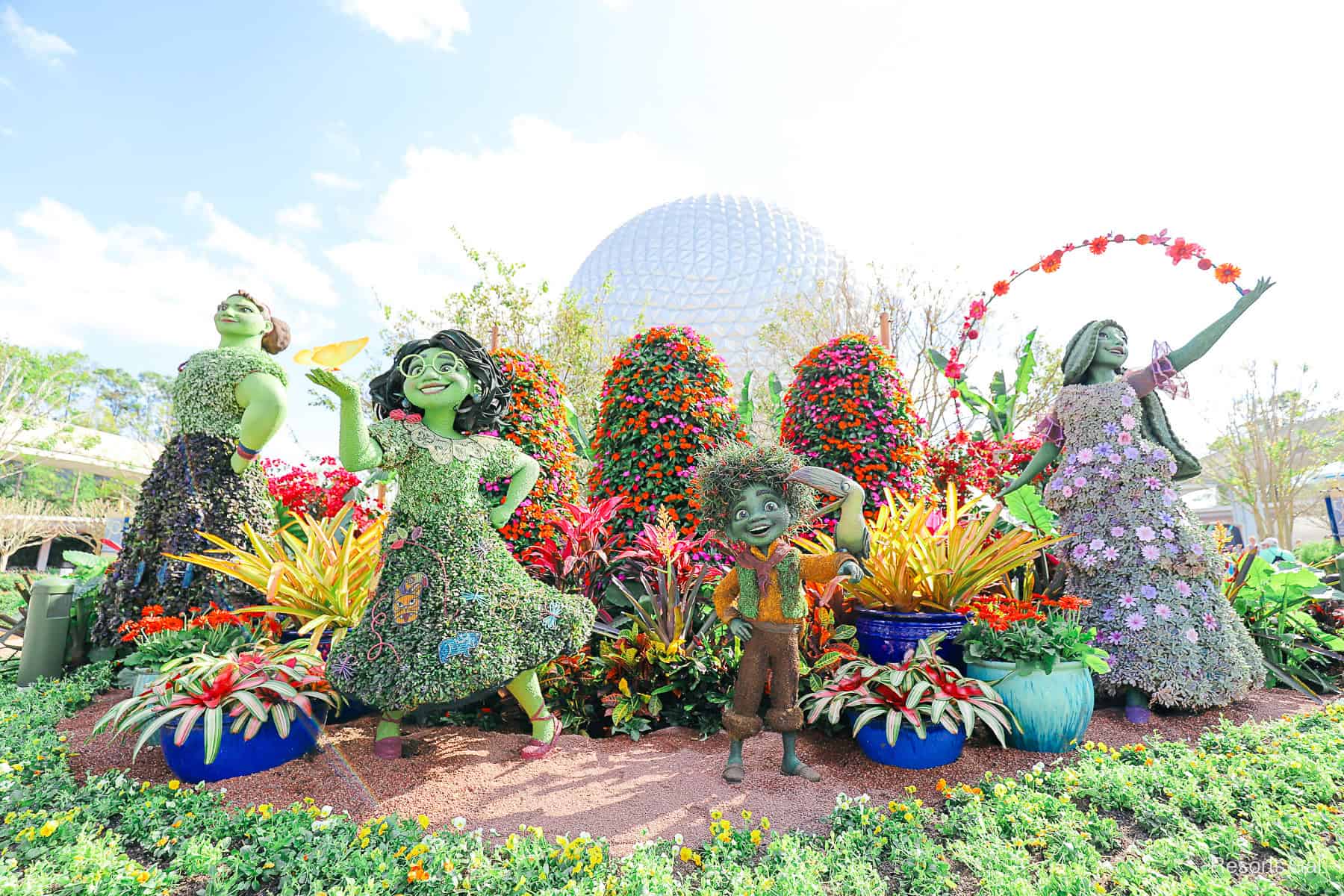 the Madrigal family covered surrounded by potted plants with Spaceship Earth in the backdrop 