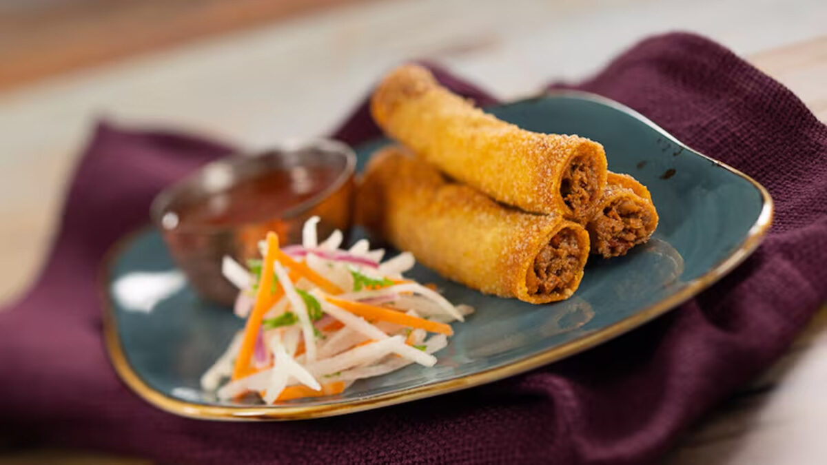 three lumpia stacked on the right side of the plate with a slaw mixture 