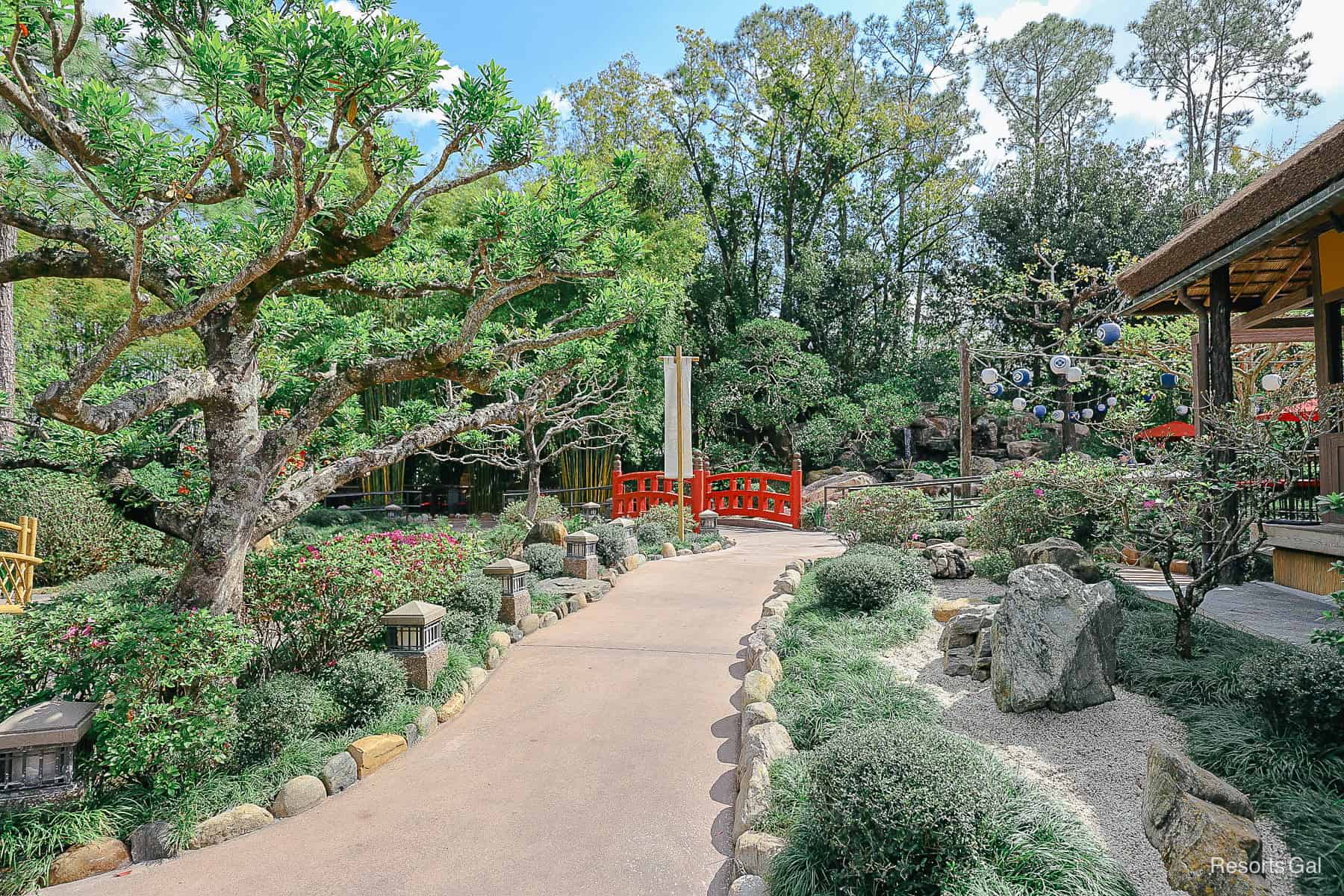 a walking path with a red bridge through the garden