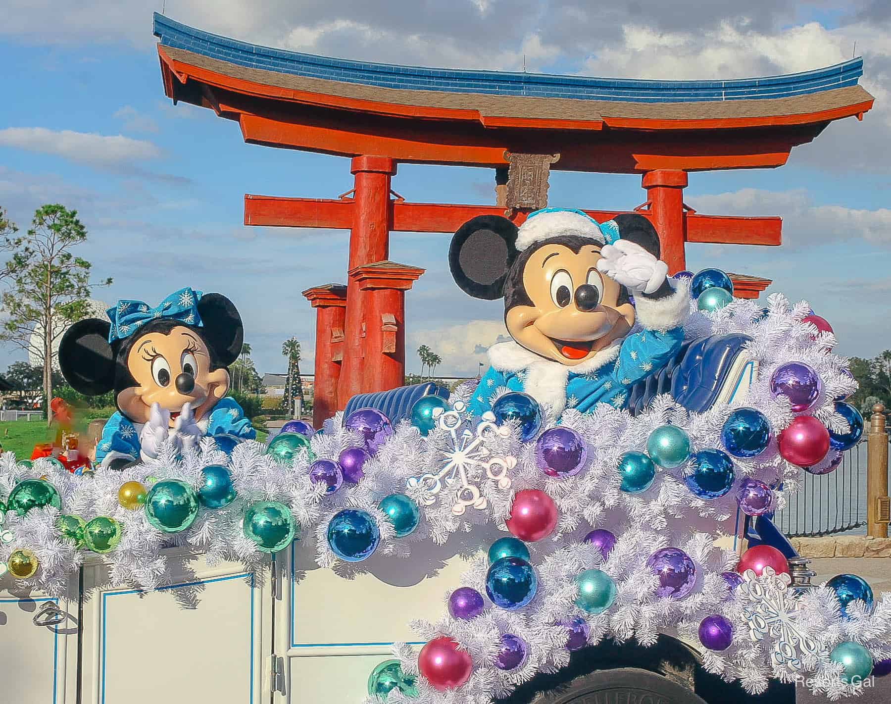 Mickey and Minnie riding in a car decorated with white and colored Christmas balls. 