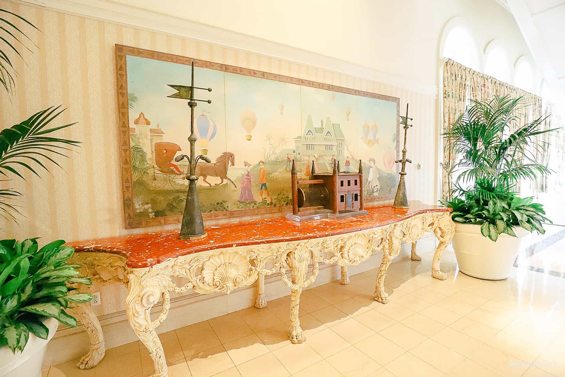 a table with a Victorian painting flanked by potted plants 