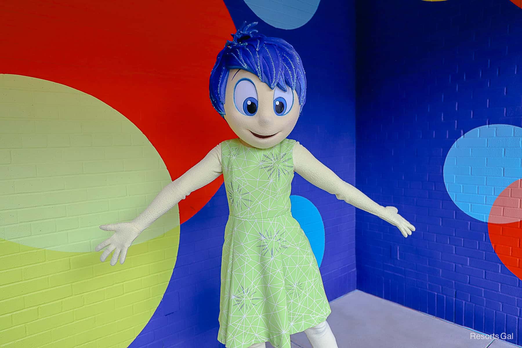 Joy poses in front of a bright blue wall at Pixar Plaza at Disney's Hollywood Studios 