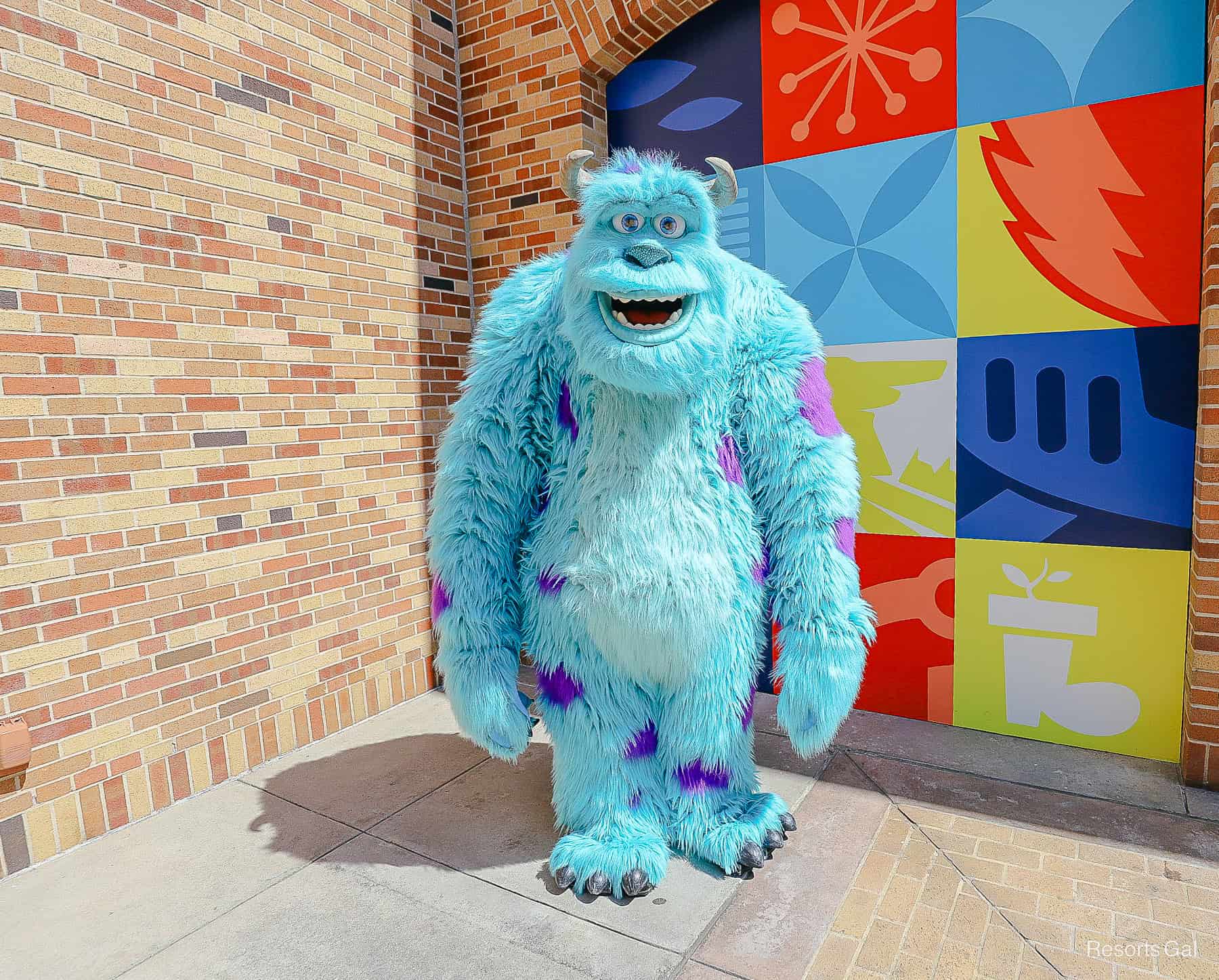 Sulley poses for a photo at Disney's Hollywood Studios near a Pixar themed wall. 