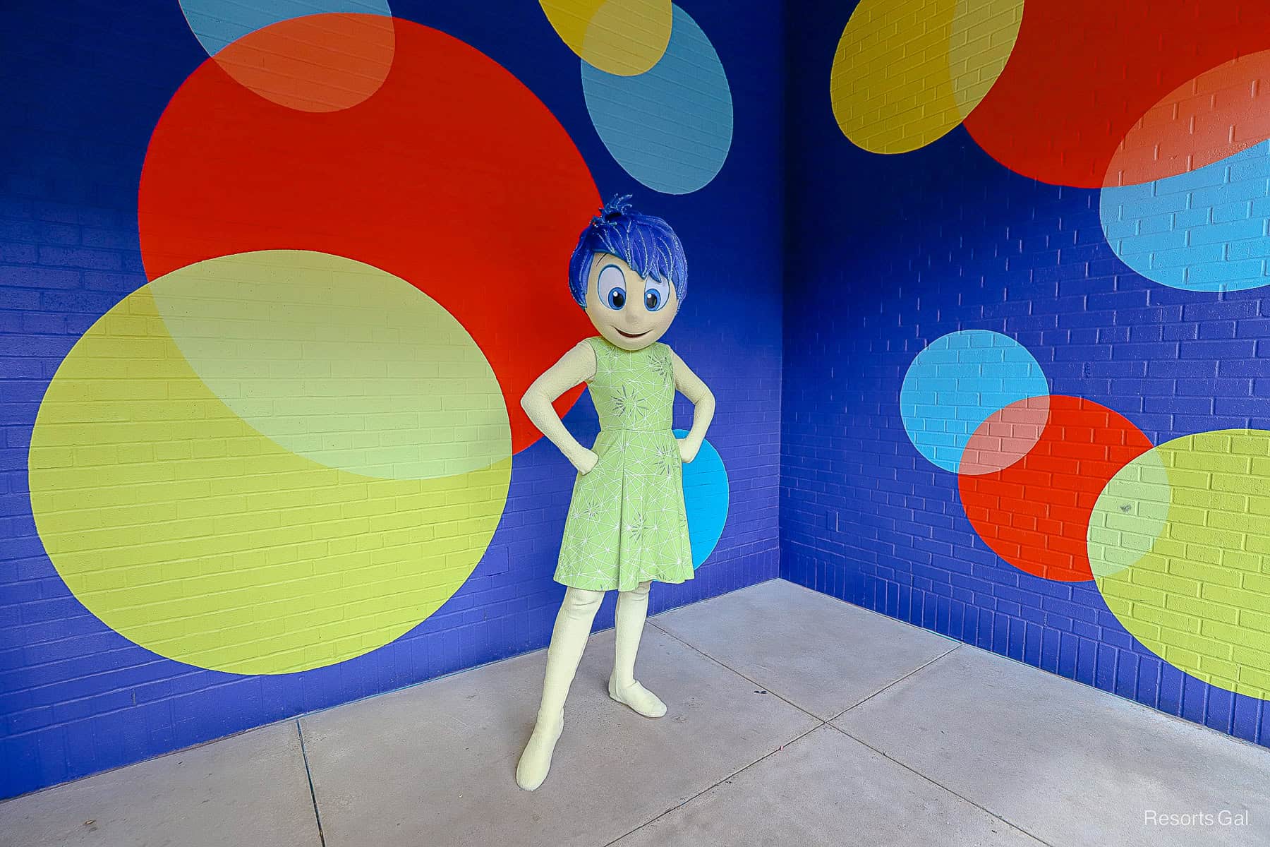 Joy poses with hands on her hips. She has blue hair and a green dress. 