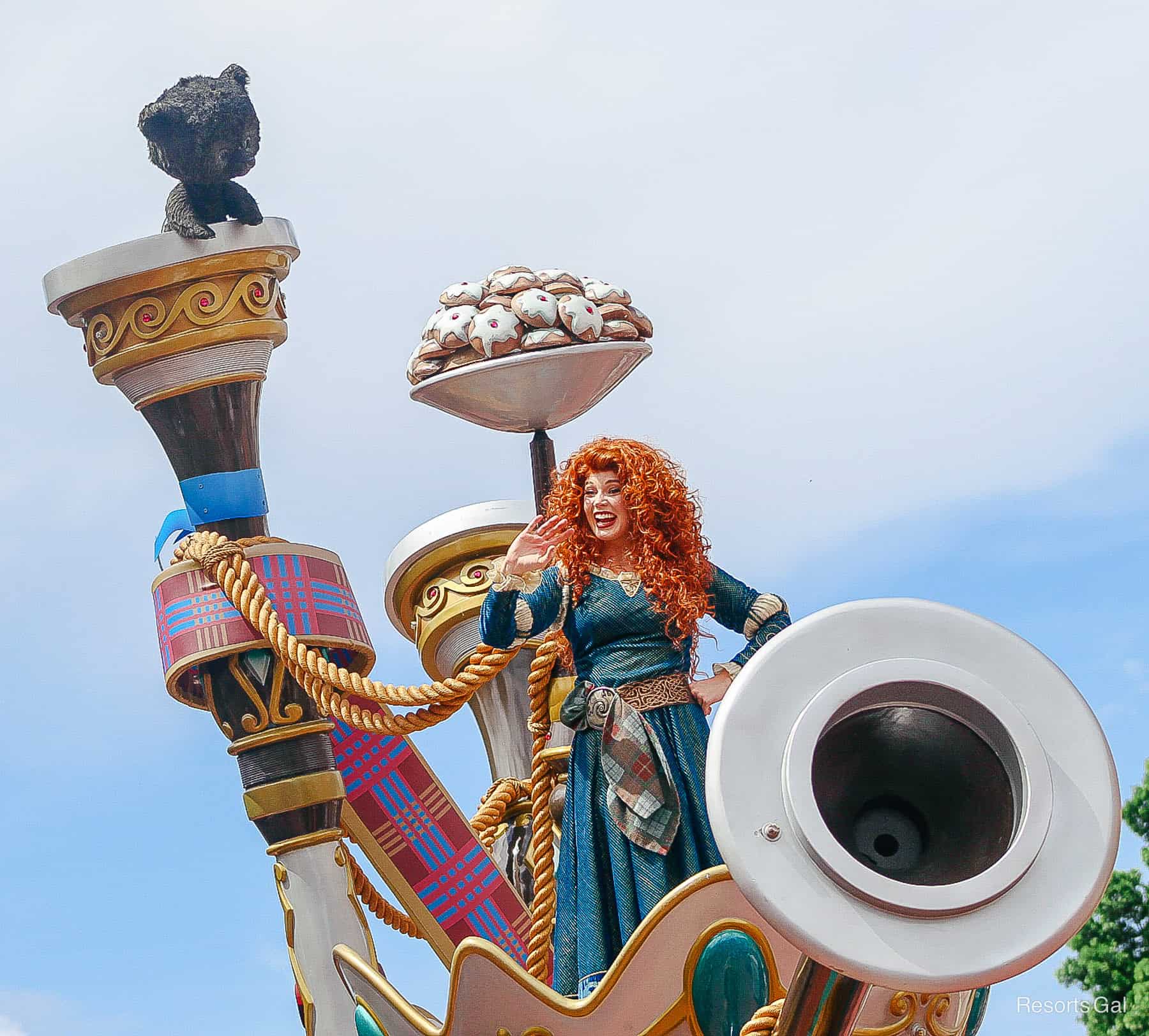 waves to guest from the perch of her float in the parade at Magic Kingdom 