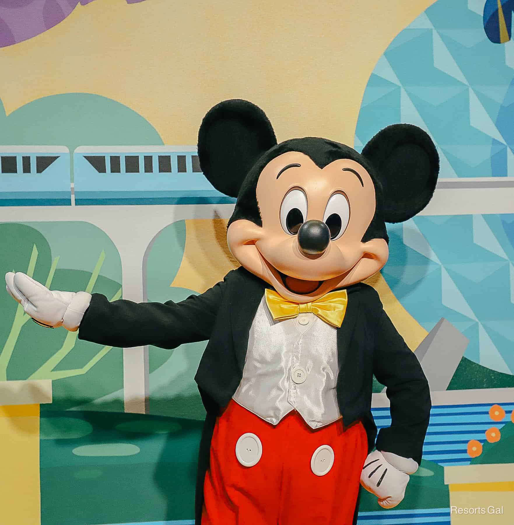 Mickey Mouses poses with a hand on hip and one arm extended. 