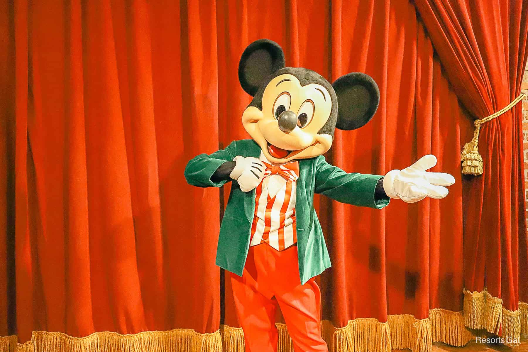 Mickey Mouse in his Christmas suit which is a candy cane striped vest and bow time, green velvet jacket and red pants. 