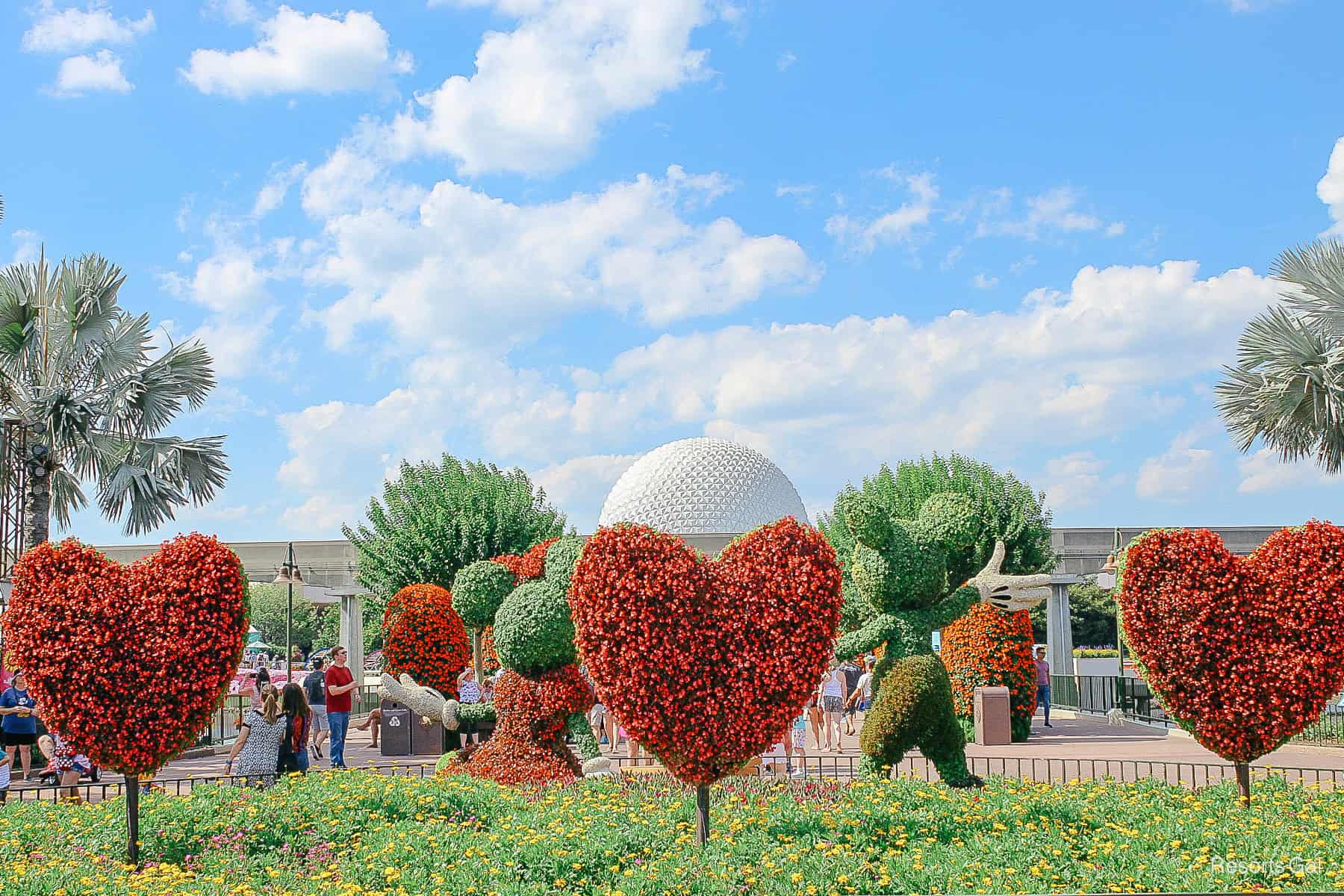 Mickey and Minnie with three heart topiaries and a blue sky backdrop 