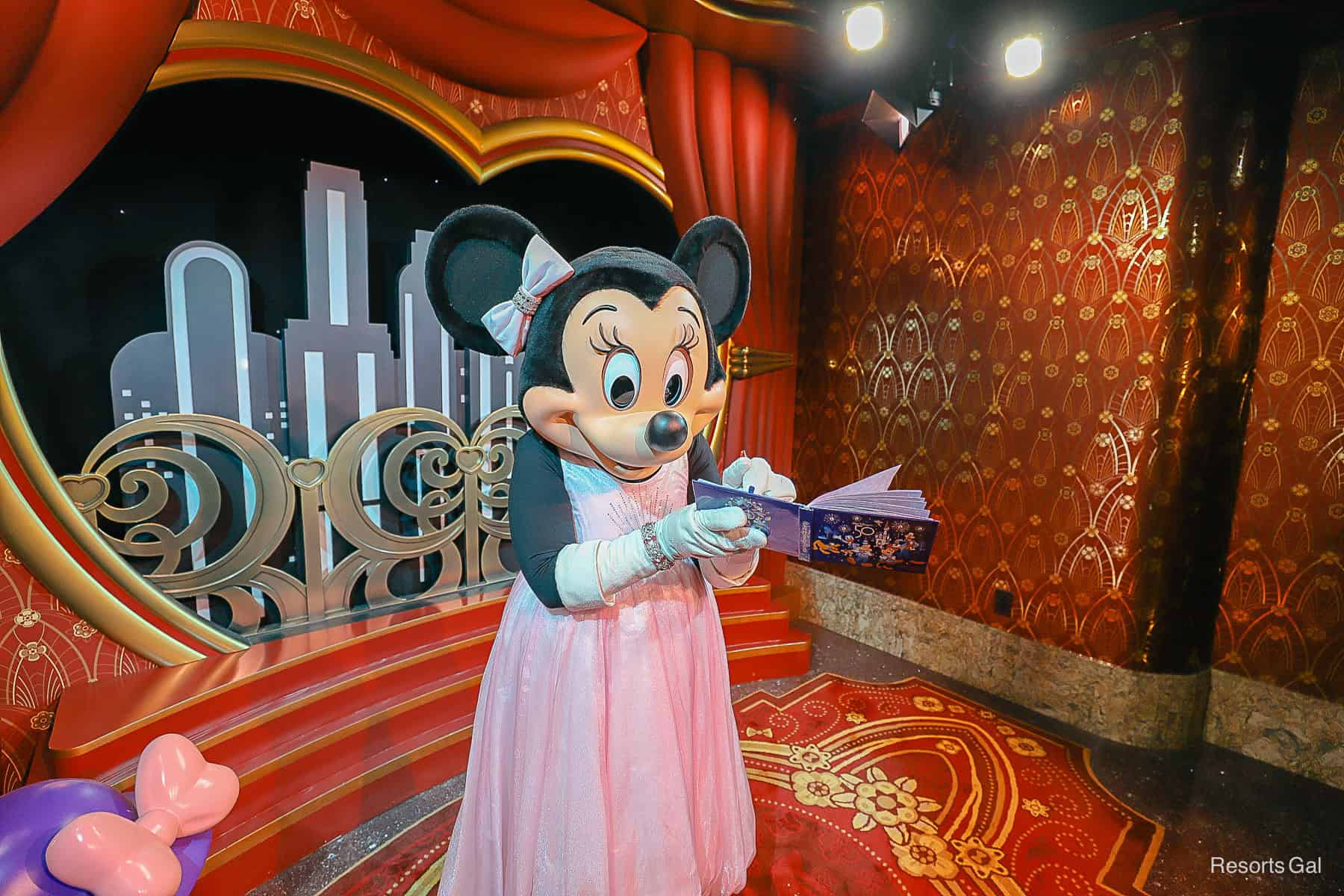 Minnie is signing her character autograph. She's wearing long white satin gloves. 