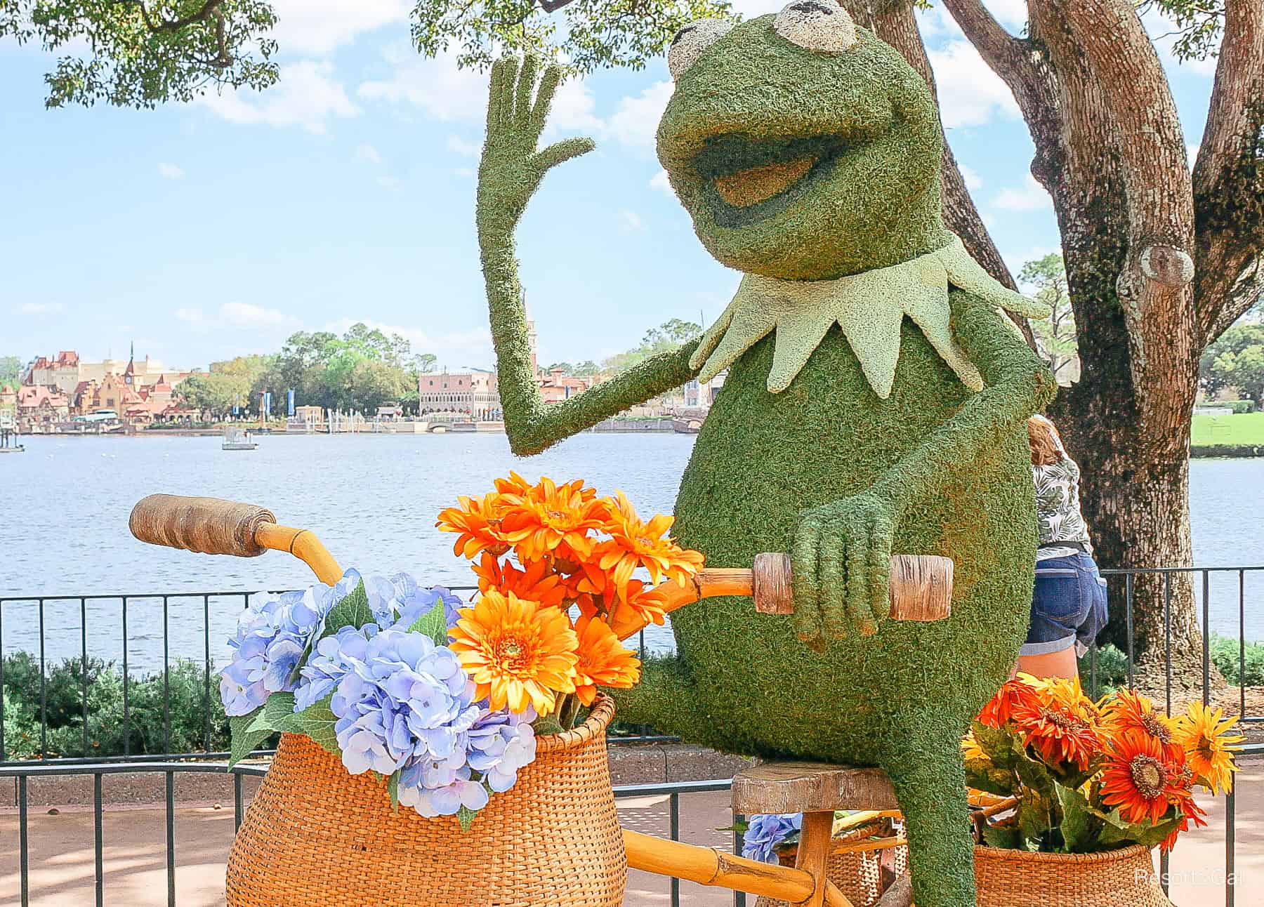 Kermit waves from his bike with a basket of flowers in topiary form. 