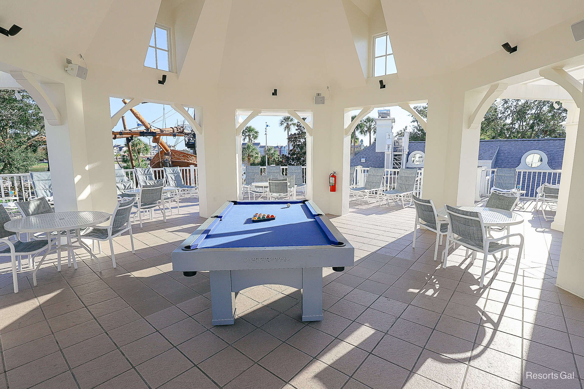 a raised deck near the pool with a game table and tables and chairs surrounding it 