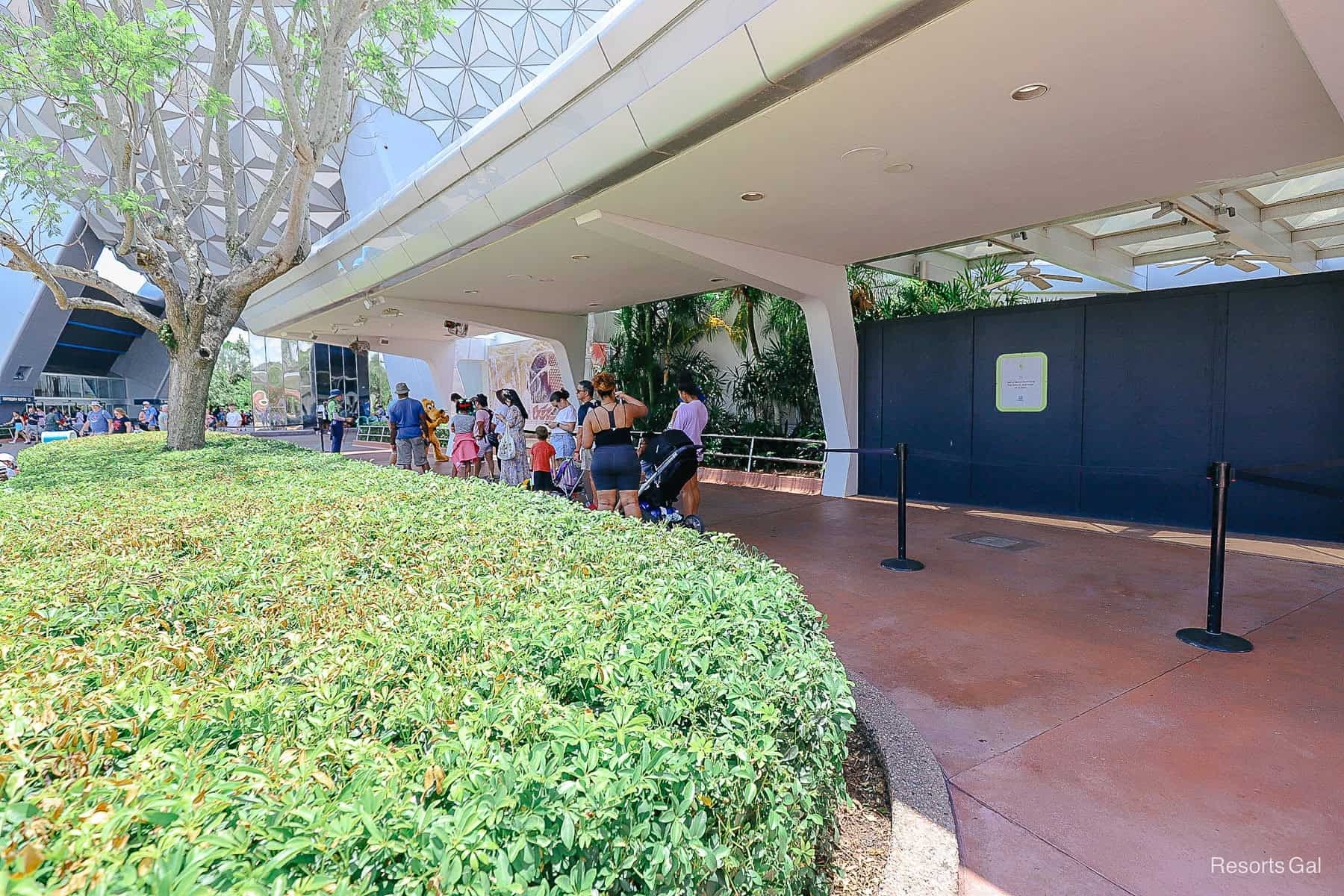 guests waiting in a partially covered area to meet Pluto at Epcot's main entrance 