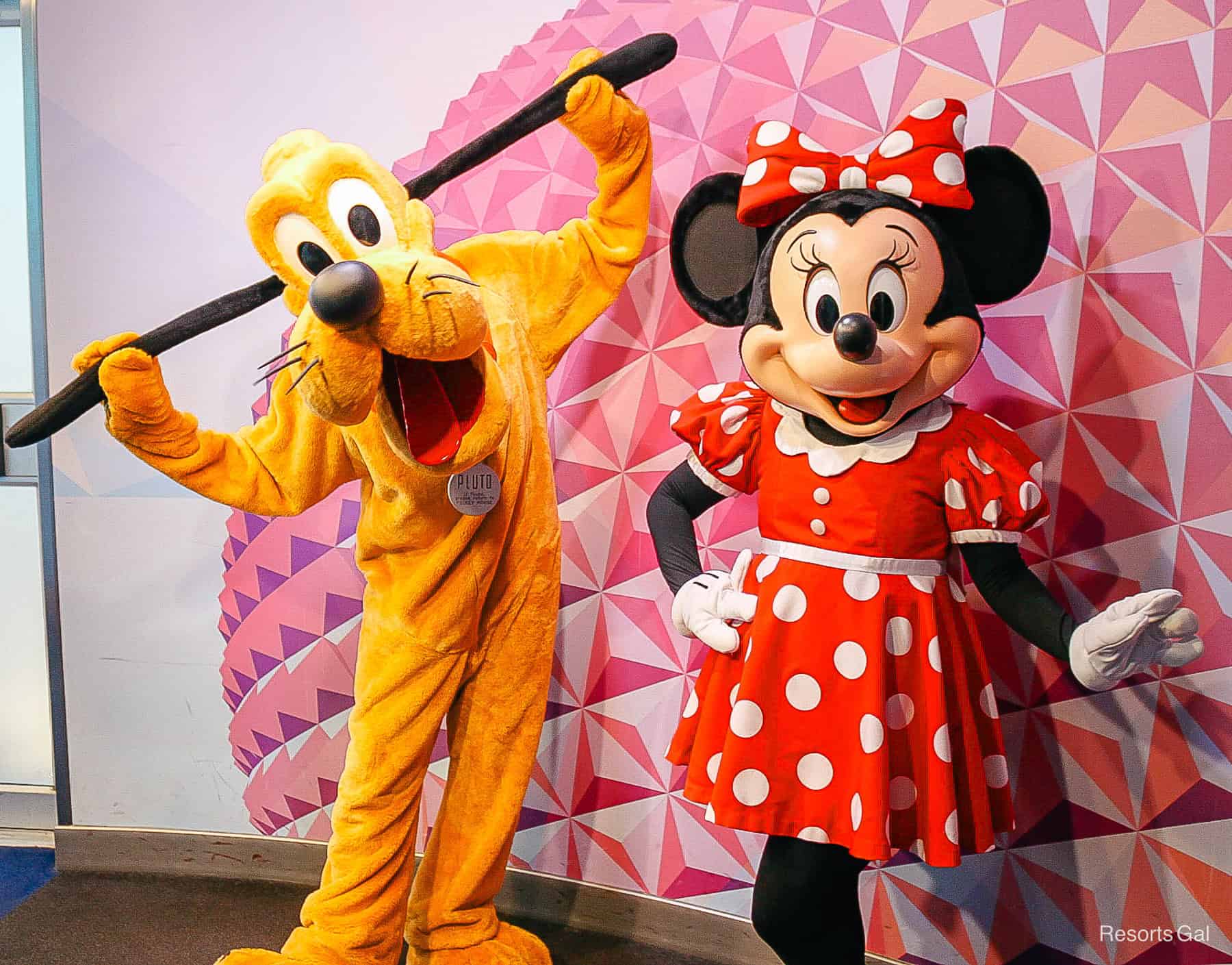 Pluto holds out his ears next to Minnie in her red-white dress. 