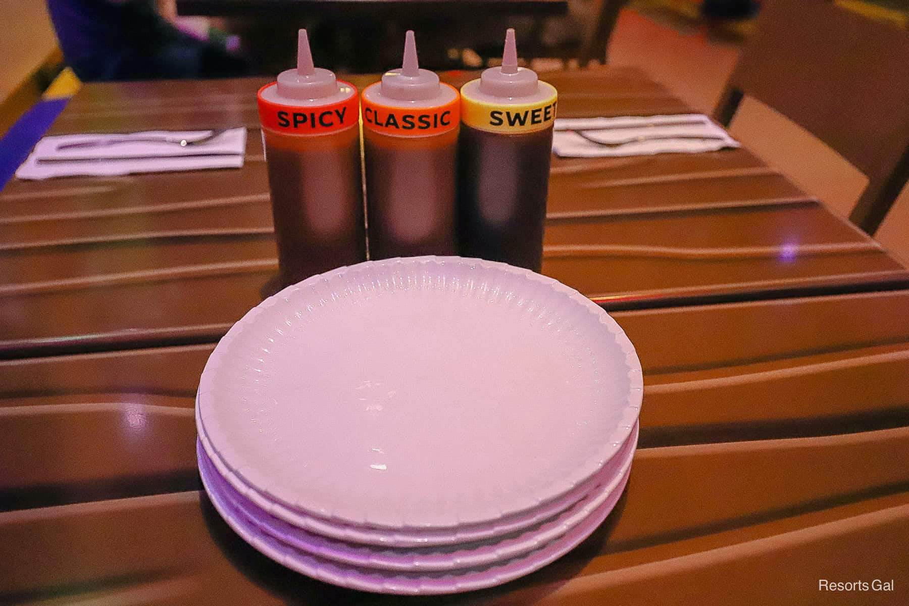 a stack of glass plates that look like paper plates and three types of BBQ sauces 