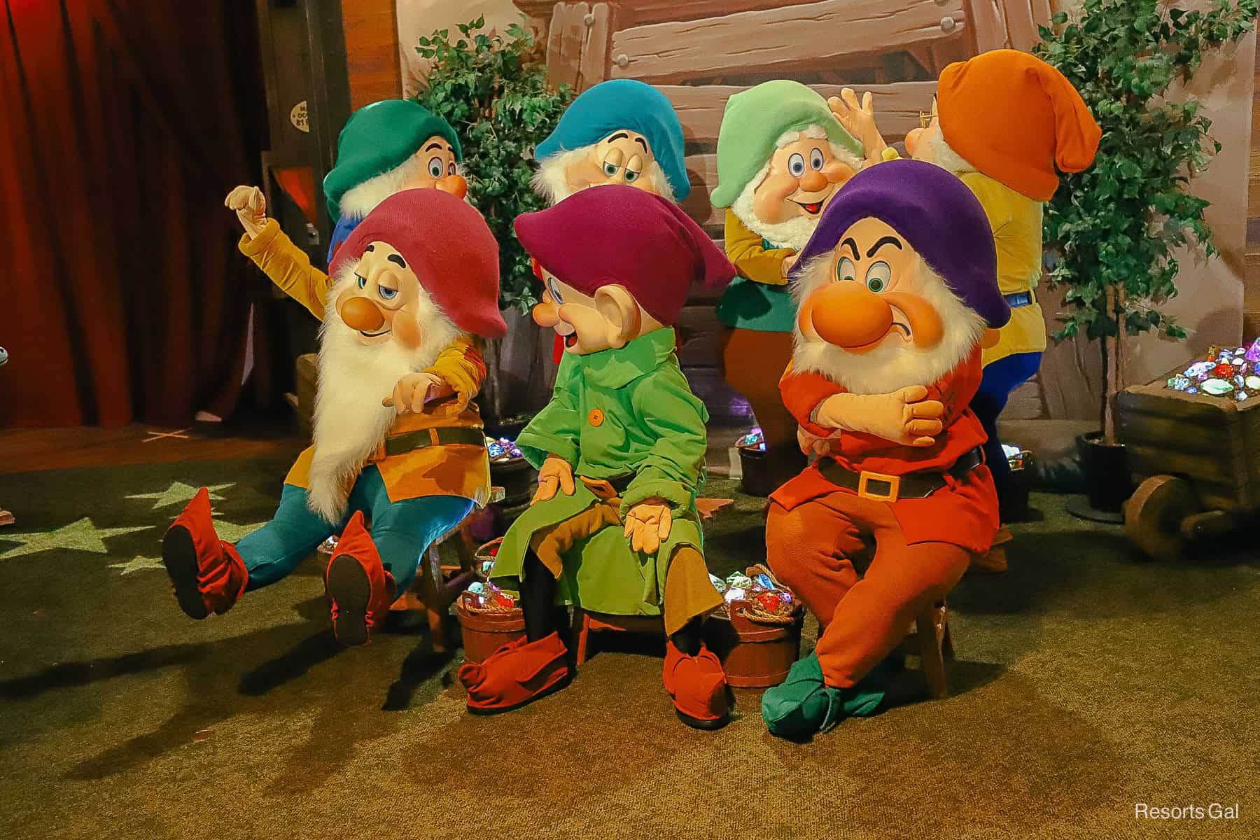 The Seven Dwarfs pose with buckets of jewels around them. 