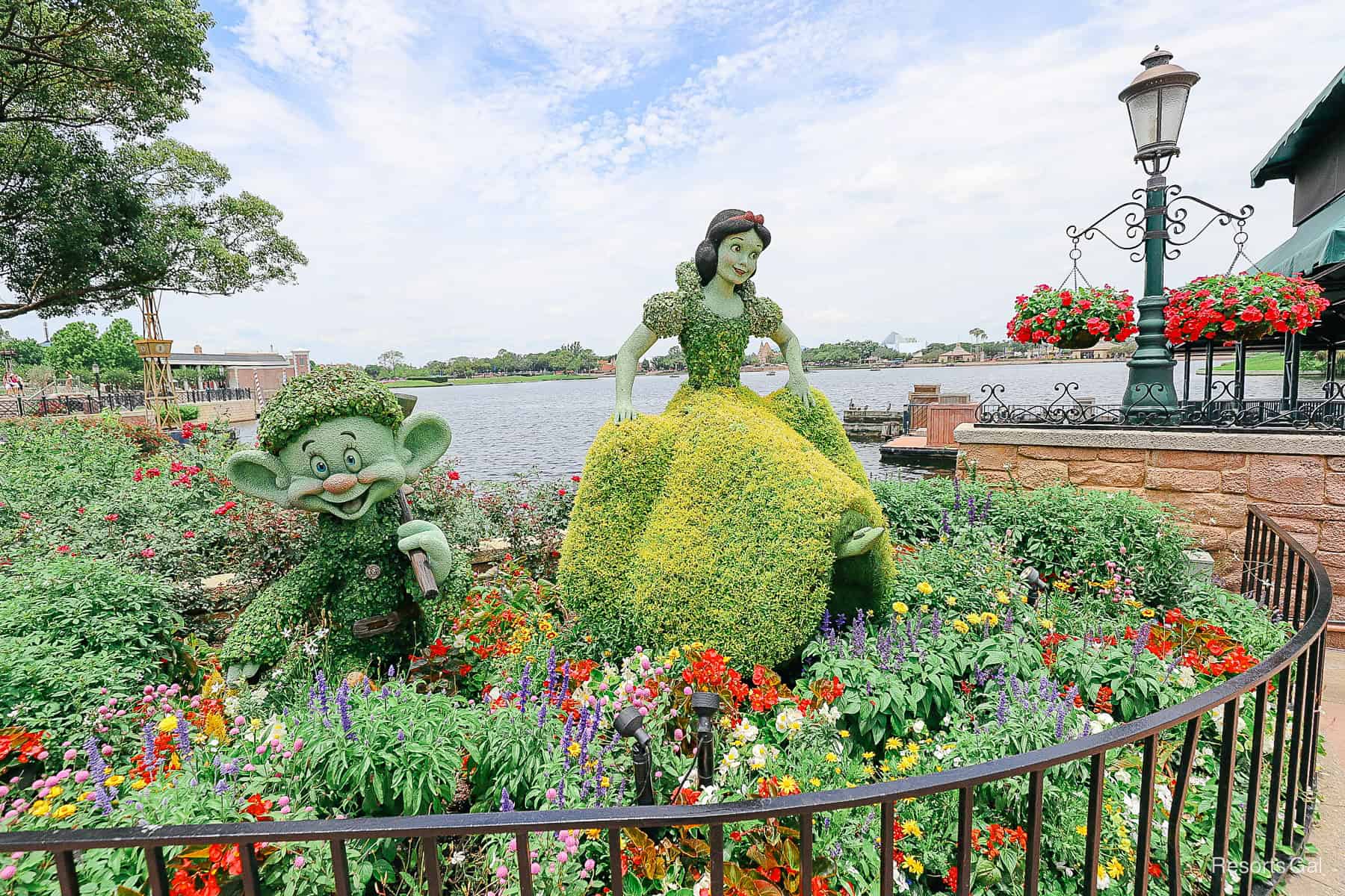 Topiary: Dopey (left) and Snow White (right) surrounded by vibrant flowers with the lagoon behind them. 