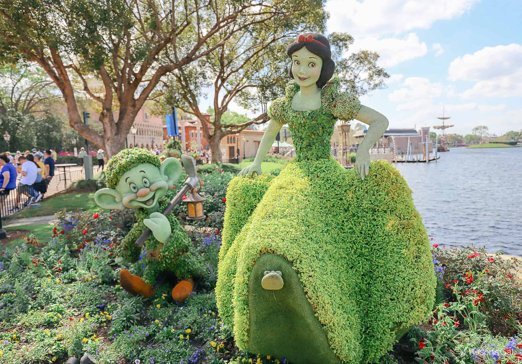 Snow White with Dopey by her side in topiary form. Her shoe looks like it's sticking out of her dress and she has a bright red bow in her hair.