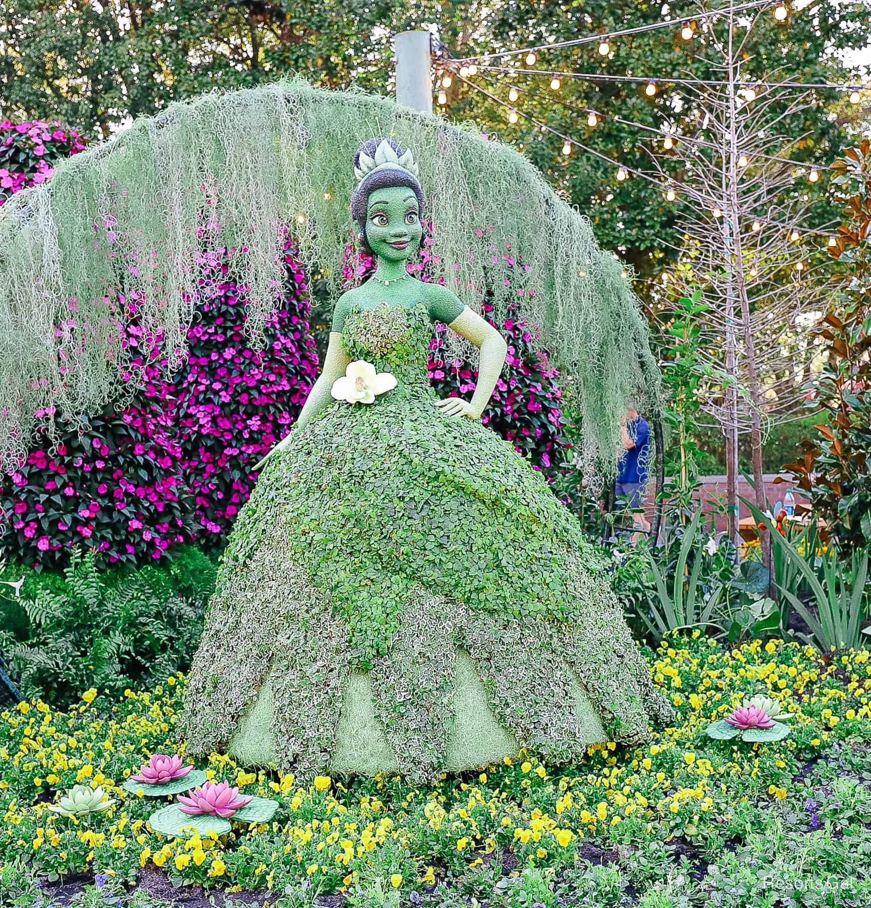 Lily pads with blooming pink flowers surround the base of Tiana's topiary. 