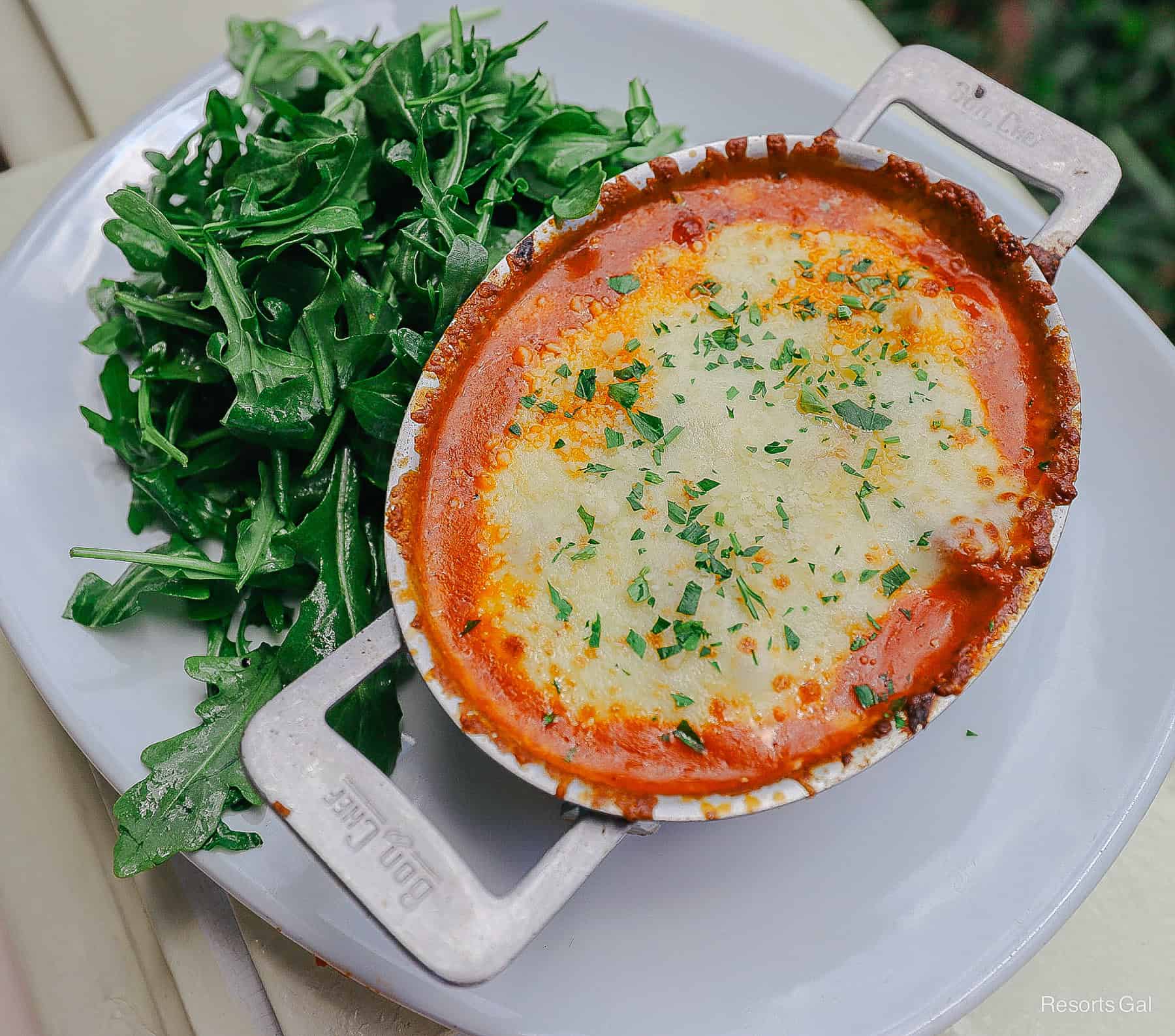 a plate with an Arugula Salad and a small casserole dish topped with parsley, cheese, and tomato sauce at Tony's 
