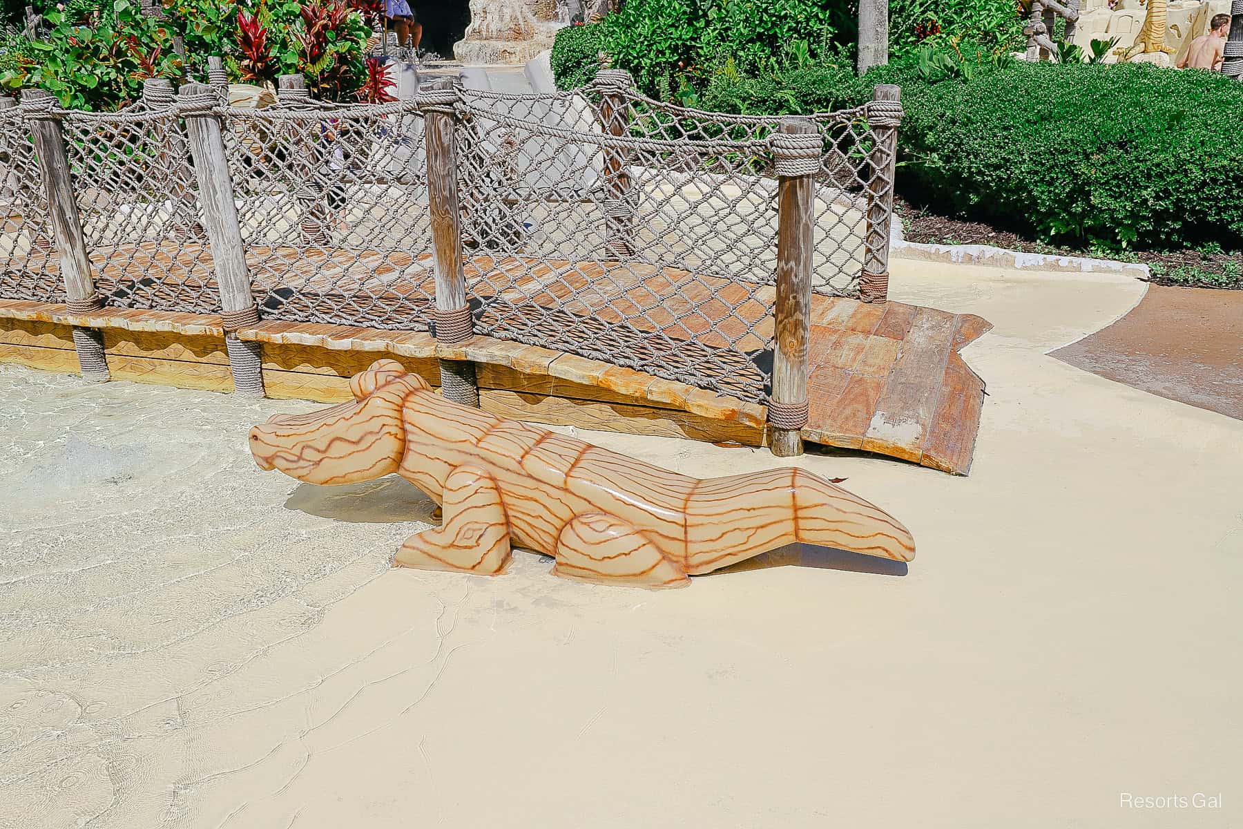 a wooden alligator play area in the splash pad with a small bridge behind it 